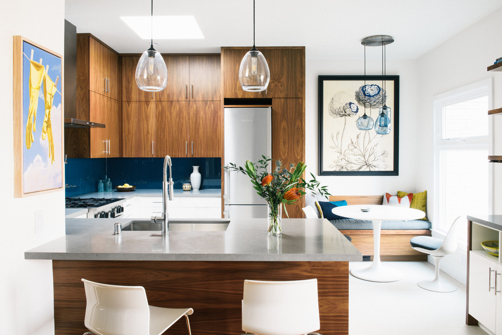 Modern inredning av ett grå grått kök, med en undermonterad diskho, släta luckor, skåp i mörkt trä, blått stänkskydd, glaspanel som stänkskydd, rostfria vitvaror, en halv köksö och vitt golv