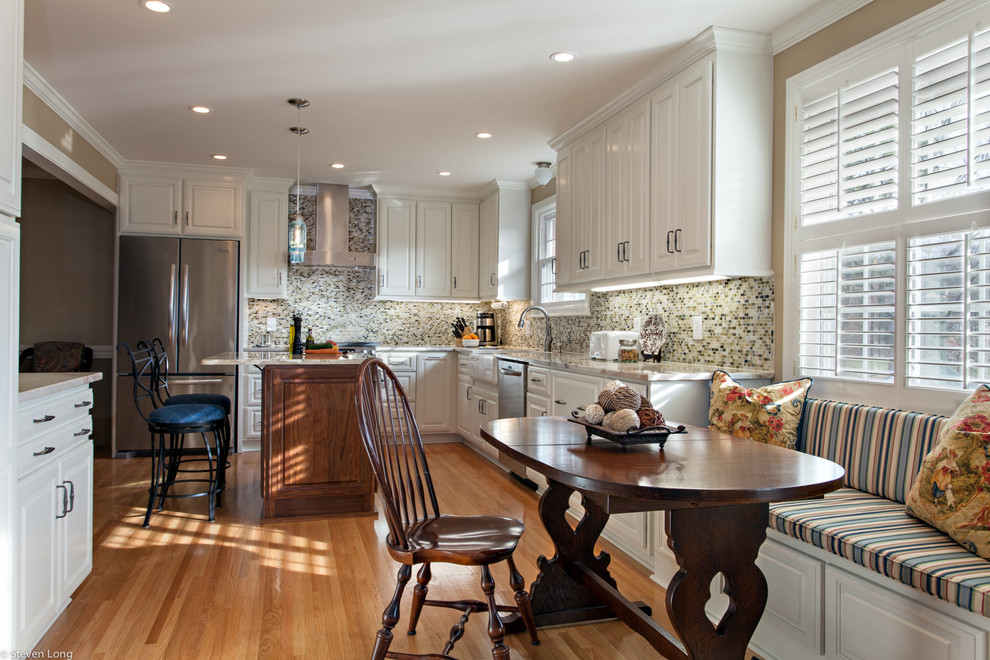 Example of a classic l-shaped medium tone wood floor eat-in kitchen design in Nashville with a farmhouse sink, raised-panel cabinets, white cabinets, granite countertops, multicolored backsplash, stainless steel appliances, mosaic tile backsplash and an island