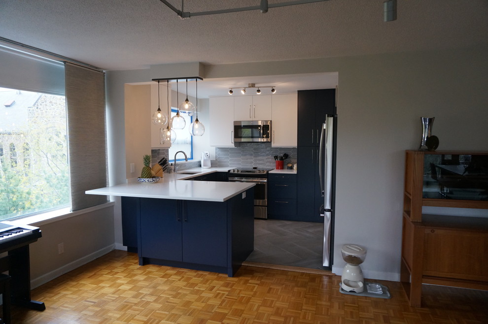Small trendy u-shaped gray floor eat-in kitchen photo in Boston with a drop-in sink, flat-panel cabinets, blue cabinets, quartz countertops, gray backsplash, glass tile backsplash, stainless steel appliances and a peninsula