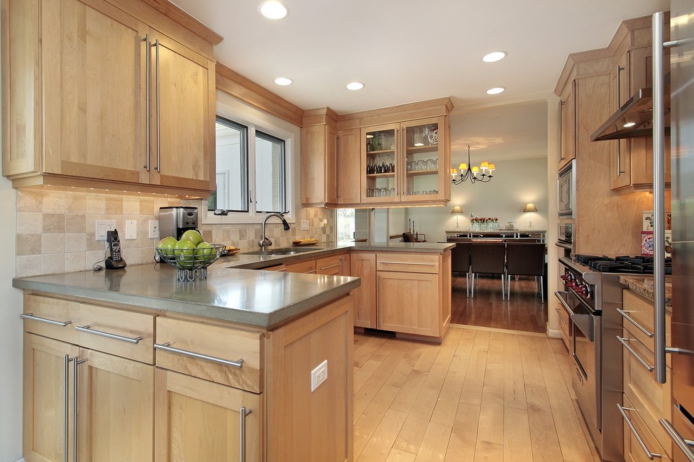Modelo de cocina actual con armarios estilo shaker, puertas de armario de madera clara, salpicadero beige y electrodomésticos de acero inoxidable
