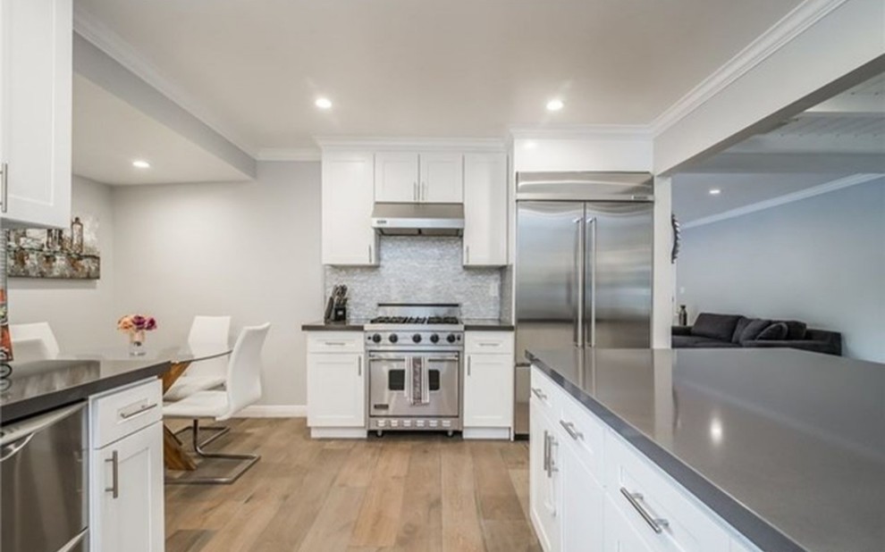 Mid-sized transitional l-shaped light wood floor and brown floor eat-in kitchen photo in Los Angeles with an island, an undermount sink, shaker cabinets, white cabinets, quartz countertops, multicolored backsplash, matchstick tile backsplash, stainless steel appliances and gray countertops