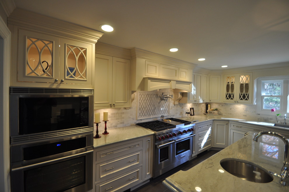 Klassisk inredning av ett kök, med en undermonterad diskho, luckor med profilerade fronter, vita skåp, bänkskiva i koppar, flerfärgad stänkskydd, stänkskydd i tunnelbanekakel och rostfria vitvaror