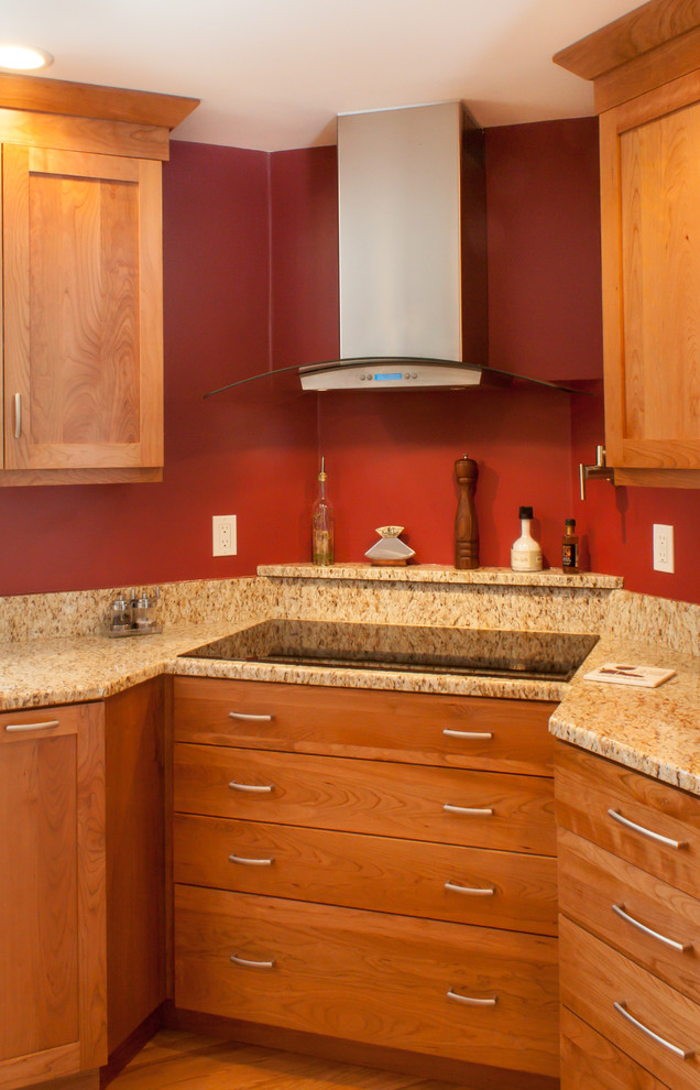 Klassisk inredning av ett kök, med en undermonterad diskho, luckor med infälld panel, skåp i mellenmörkt trä, granitbänkskiva, rött stänkskydd och rostfria vitvaror