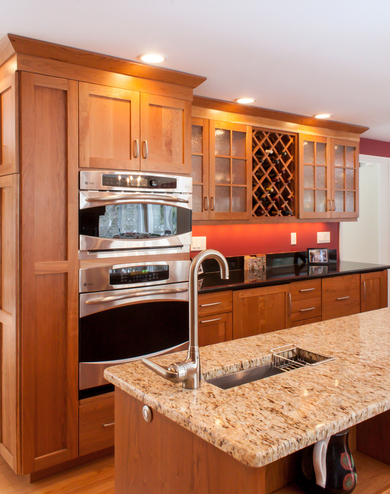 Exemple d'une cuisine américaine chic en L et bois brun avec un évier encastré, un placard avec porte à panneau encastré, un plan de travail en granite, une crédence rouge et un électroménager en acier inoxydable.