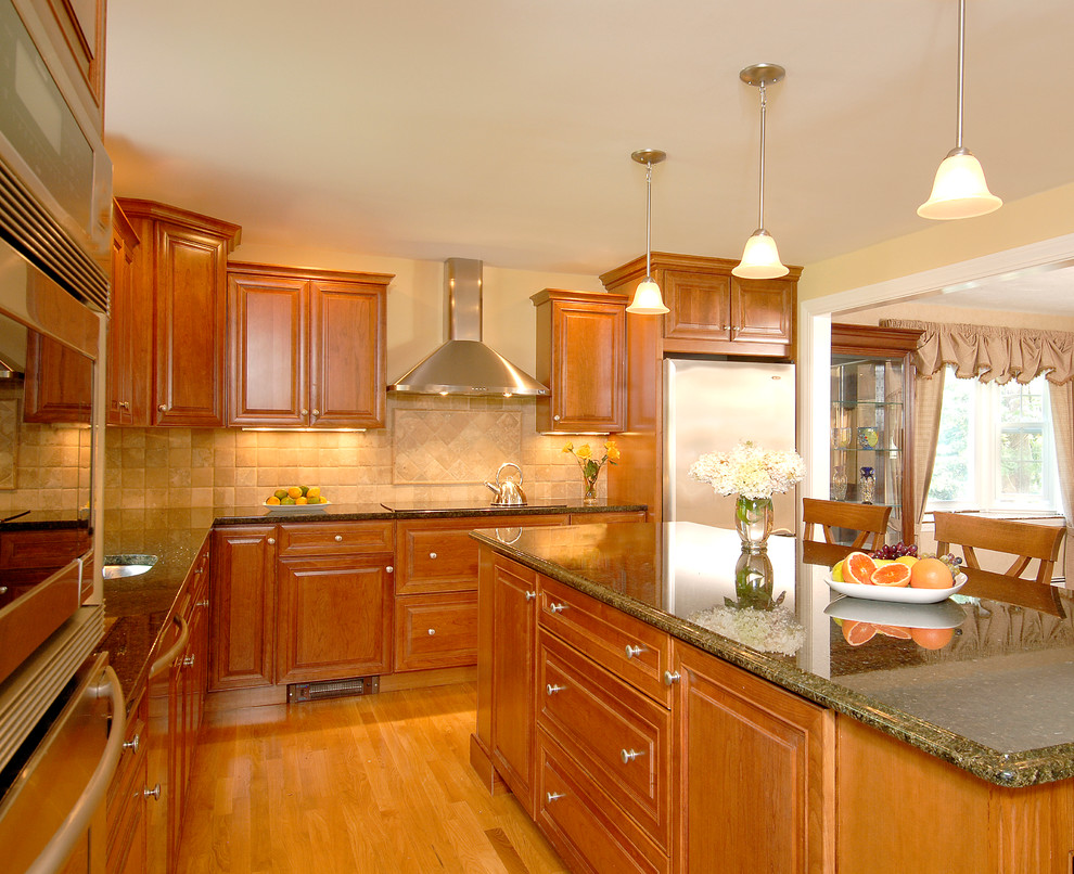 This is an example of a medium sized contemporary l-shaped kitchen/diner in Boston with a built-in sink, recessed-panel cabinets, medium wood cabinets, granite worktops, beige splashback, cement tile splashback, stainless steel appliances, light hardwood flooring and an island.