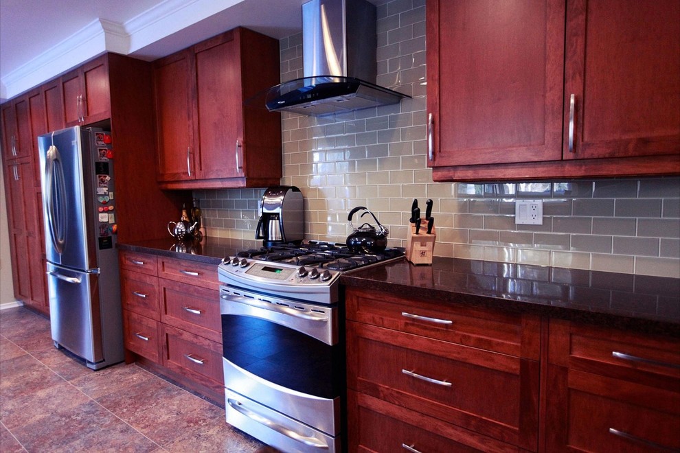 Klassisk inredning av ett kök, med en undermonterad diskho, luckor med infälld panel, skåp i mellenmörkt trä, bänkskiva i kvartsit, brunt stänkskydd, stänkskydd i glaskakel, rostfria vitvaror och vinylgolv
