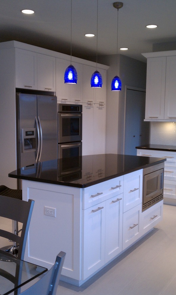 Foto de cocina actual, de tamaño medio, con puertas de armario blancas, electrodomésticos de acero inoxidable, una isla, armarios con paneles empotrados, encimera de granito, salpicadero blanco y salpicadero de azulejos de cerámica