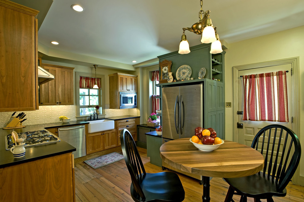 Bild på ett mellanstort lantligt kök, med en rustik diskho, släta luckor, skåp i mellenmörkt trä, bänkskiva i täljsten, vitt stänkskydd, stänkskydd i metallkakel, rostfria vitvaror och ljust trägolv