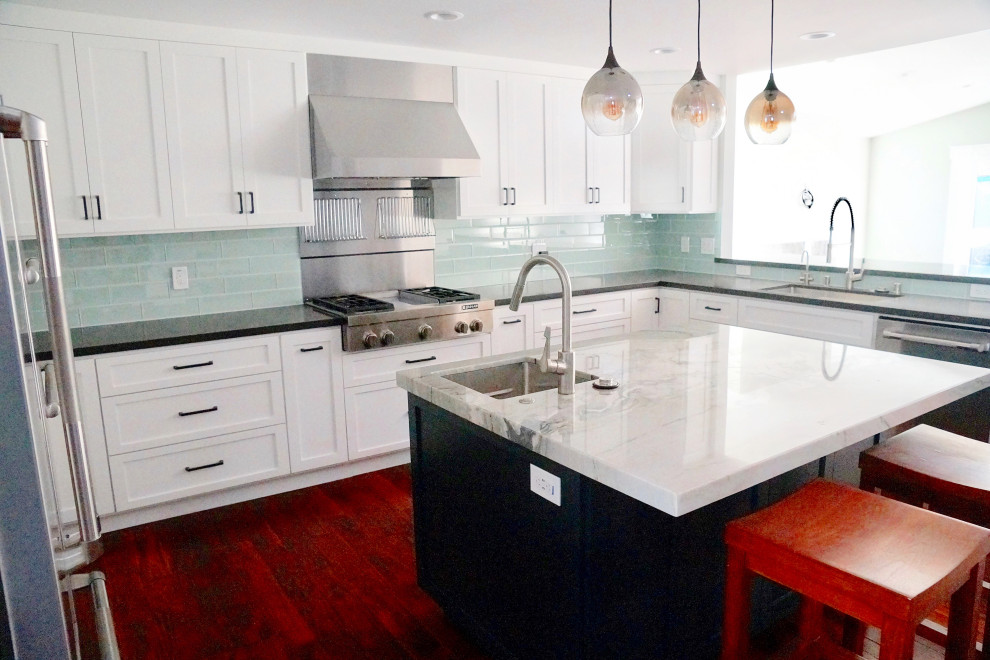 Modern inredning av ett avskilt, stort vit vitt u-kök, med en undermonterad diskho, skåp i shakerstil, vita skåp, granitbänkskiva, blått stänkskydd, stänkskydd i glaskakel, rostfria vitvaror, mörkt trägolv, en köksö och rött golv