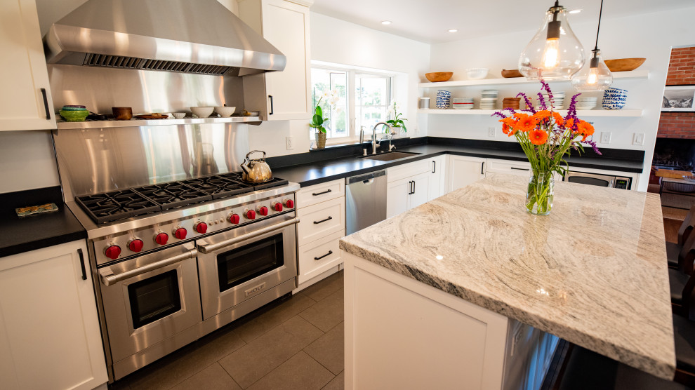 Inspiration for a classic kitchen in Santa Barbara with a belfast sink, shaker cabinets, white cabinets, granite worktops, stainless steel appliances, brown floors and black worktops.