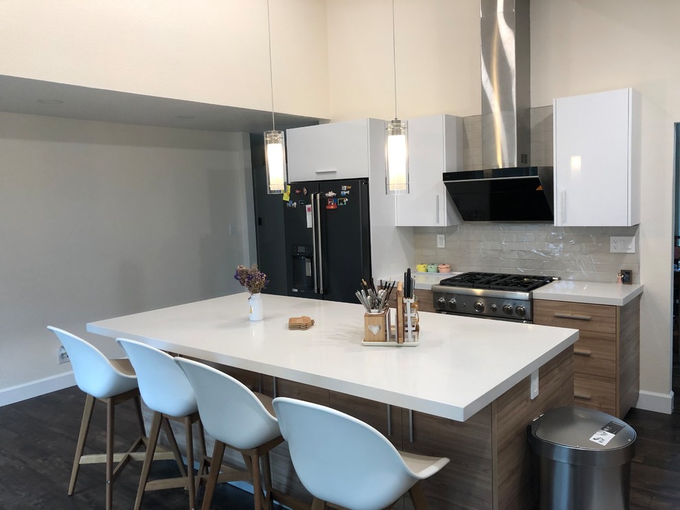 This is an example of a medium sized modern l-shaped enclosed kitchen in San Francisco with a submerged sink, quartz worktops, beige splashback, glass tiled splashback, black appliances, laminate floors, an island, white worktops, flat-panel cabinets, white cabinets and brown floors.