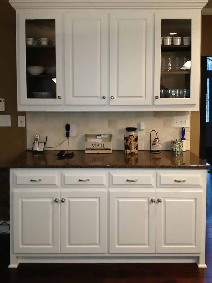 Cette image montre une cuisine américaine traditionnelle en L avec un évier 2 bacs, un placard avec porte à panneau surélevé, des portes de placard blanches, un plan de travail en granite, une crédence blanche, une crédence en céramique et un électroménager en acier inoxydable.
