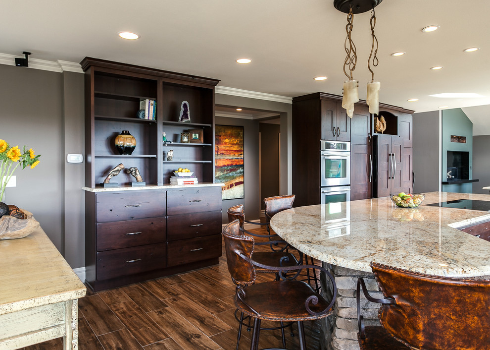Open concept kitchen - large traditional u-shaped medium tone wood floor open concept kitchen idea in Denver with dark wood cabinets, granite countertops, beige backsplash, stone tile backsplash, stainless steel appliances, an undermount sink, flat-panel cabinets and an island