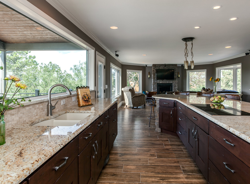 Open concept kitchen - large traditional u-shaped medium tone wood floor open concept kitchen idea in Denver with dark wood cabinets, granite countertops, beige backsplash, stone tile backsplash, stainless steel appliances, an undermount sink, flat-panel cabinets and an island