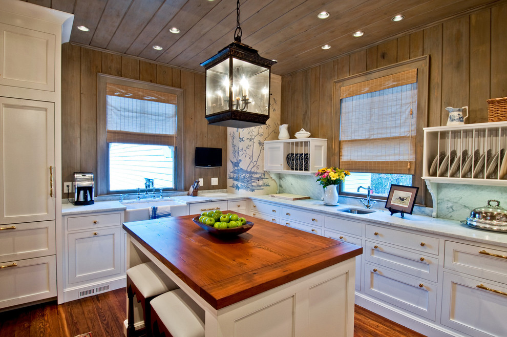 Inredning av ett kök, med träbänkskiva, integrerade vitvaror, en rustik diskho, luckor med infälld panel och vita skåp