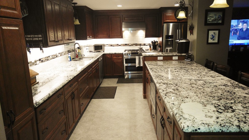Example of a large classic l-shaped concrete floor and beige floor open concept kitchen design in Boston with an undermount sink, raised-panel cabinets, dark wood cabinets, granite countertops, white backsplash, subway tile backsplash, stainless steel appliances, an island and white countertops