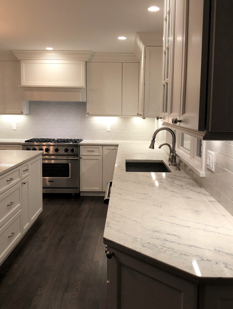 Inspiration for a large contemporary painted wood floor and brown floor kitchen remodel in New York with an undermount sink, recessed-panel cabinets, white cabinets, granite countertops, ceramic backsplash, stainless steel appliances, an island, multicolored countertops and gray backsplash