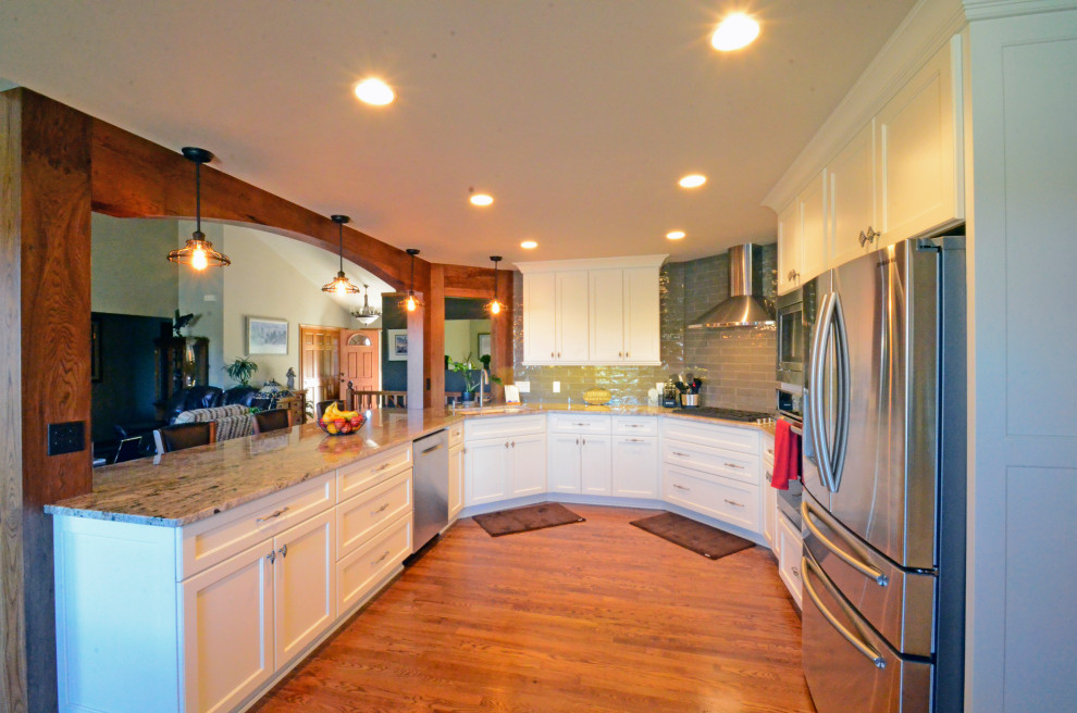 Inredning av ett klassiskt stort flerfärgad flerfärgat kök, med en rustik diskho, släta luckor, vita skåp, granitbänkskiva, grått stänkskydd, stänkskydd i porslinskakel, rostfria vitvaror, mörkt trägolv, en köksö och brunt golv