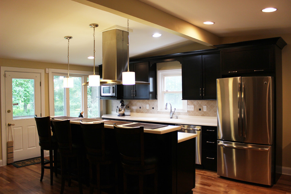 Esempio di una cucina moderna di medie dimensioni con lavello integrato, ante lisce, ante nere, top in superficie solida, paraspruzzi beige, paraspruzzi con piastrelle di vetro, elettrodomestici in acciaio inossidabile e parquet chiaro