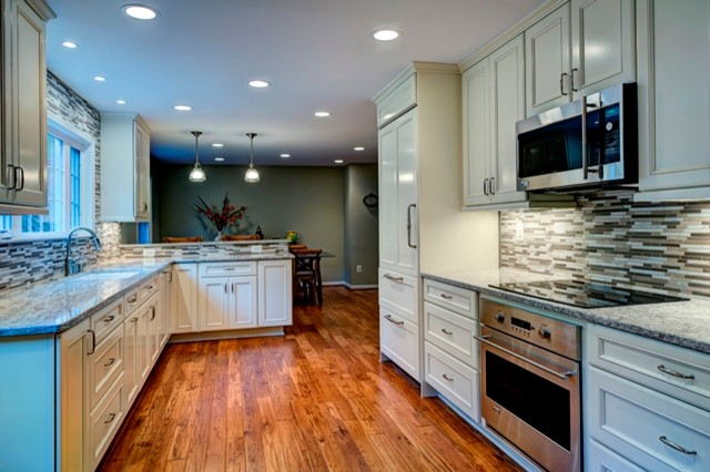 This is an example of a medium sized traditional l-shaped kitchen/diner in DC Metro with a single-bowl sink, recessed-panel cabinets, white cabinets, multi-coloured splashback, stainless steel appliances, medium hardwood flooring and engineered stone countertops.