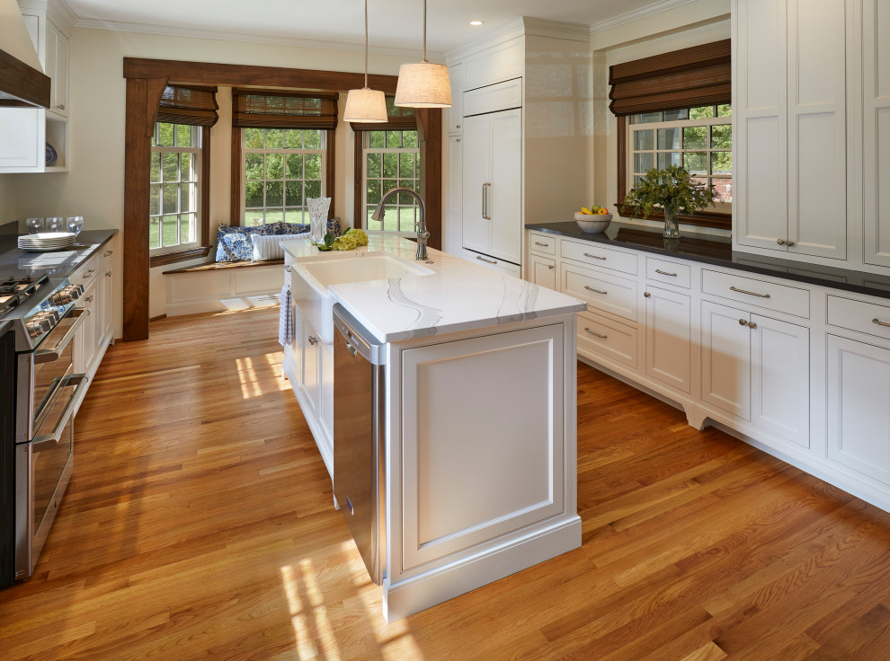 Cette photo montre une cuisine parallèle craftsman de taille moyenne avec un évier de ferme, un placard à porte affleurante, des portes de placard blanches, un plan de travail en quartz modifié et un sol en bois brun.