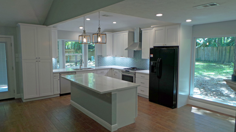 This is an example of a large traditional l-shaped open plan kitchen in Houston with a submerged sink, shaker cabinets, white cabinets, engineered stone countertops, blue splashback, glass tiled splashback, stainless steel appliances, laminate floors, an island, brown floors and white worktops.