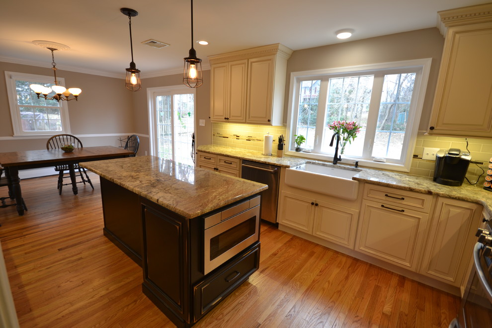 Eat-in kitchen - mid-sized traditional l-shaped light wood floor and brown floor eat-in kitchen idea in Philadelphia with a farmhouse sink, recessed-panel cabinets, white cabinets, granite countertops, beige backsplash, ceramic backsplash, stainless steel appliances and an island