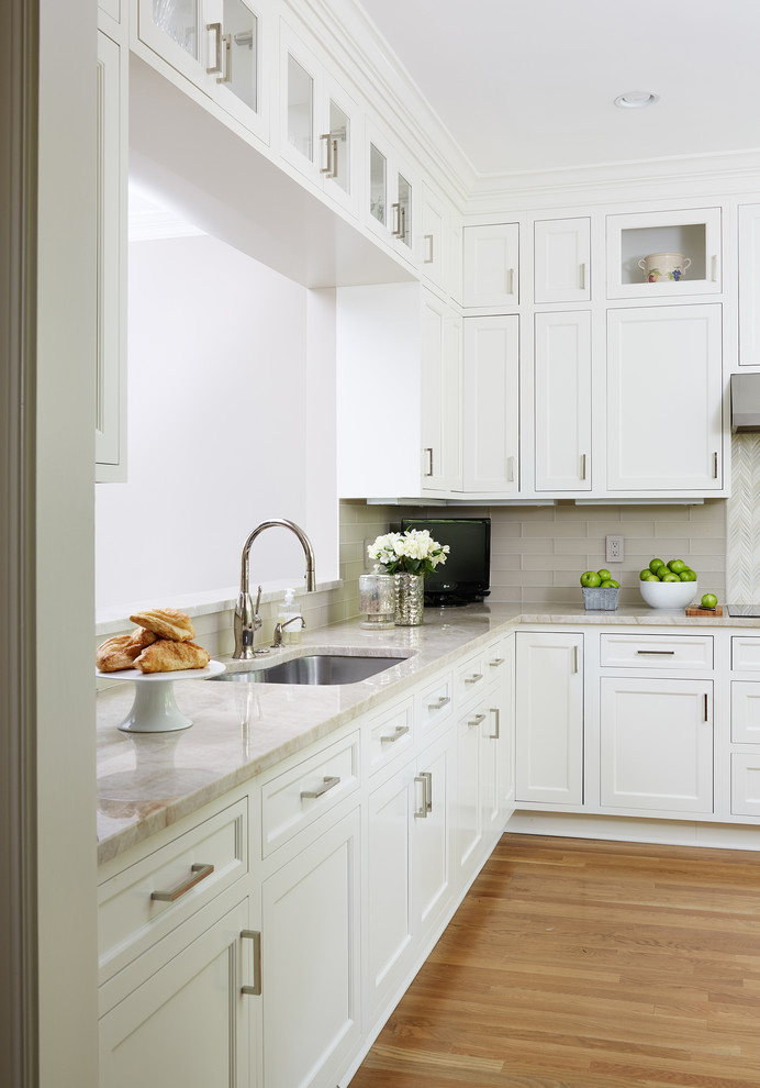 This is an example of a medium sized traditional l-shaped kitchen/diner in DC Metro with white cabinets, beige splashback, metro tiled splashback, stainless steel appliances and medium hardwood flooring.