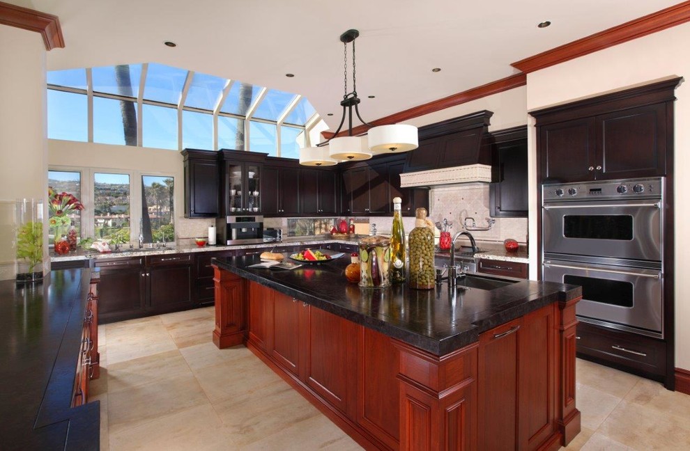 Large transitional u-shaped ceramic tile and beige floor enclosed kitchen photo in Orange County with an undermount sink, stainless steel appliances, recessed-panel cabinets, black cabinets, an island, granite countertops, beige backsplash and stone tile backsplash