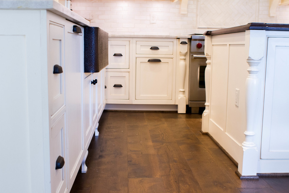 Inspiration for a country dark wood floor kitchen remodel in New York with a farmhouse sink, shaker cabinets, white cabinets, wood countertops, white backsplash, stainless steel appliances and an island