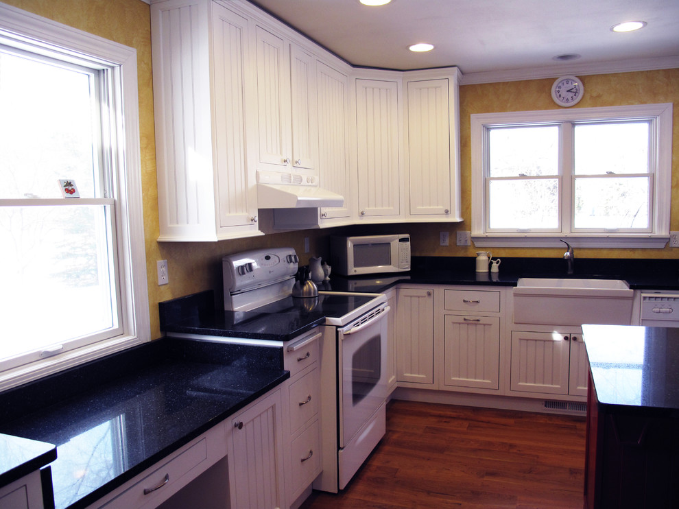 ミルウォーキーにある中くらいなカントリー風のおしゃれなキッチン (エプロンフロントシンク、インセット扉のキャビネット、白いキャビネット、御影石カウンター、黄色いキッチンパネル、白い調理設備、無垢フローリング) の写真