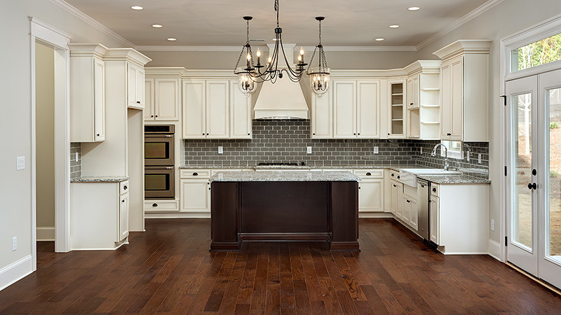 Example of a large classic u-shaped dark wood floor eat-in kitchen design in Atlanta with a farmhouse sink, recessed-panel cabinets, white cabinets, granite countertops, gray backsplash and an island