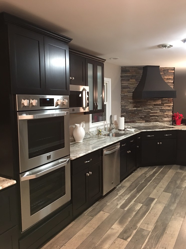 Inspiration for a mid-sized timeless l-shaped medium tone wood floor enclosed kitchen remodel in Orange County with an undermount sink, shaker cabinets, black cabinets, marble countertops, brown backsplash, stainless steel appliances, a peninsula and stone tile backsplash