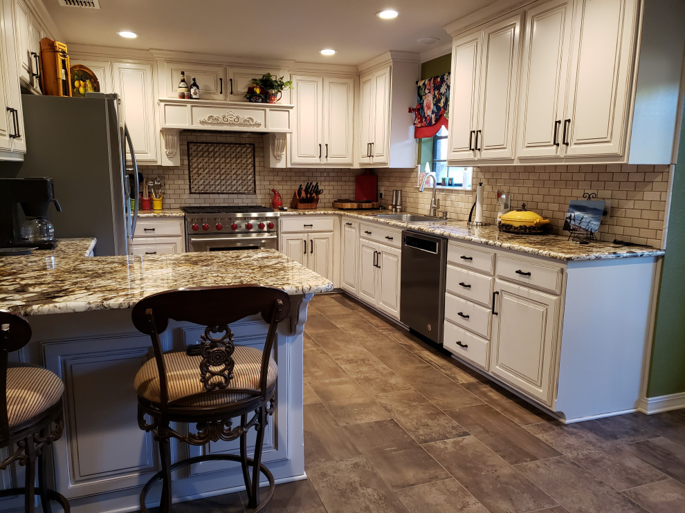 Photo of a medium sized traditional u-shaped kitchen/diner in Dallas with raised-panel cabinets, white cabinets, granite worktops, beige splashback, ceramic splashback, stainless steel appliances, ceramic flooring, no island, brown floors, multicoloured worktops and a built-in sink.