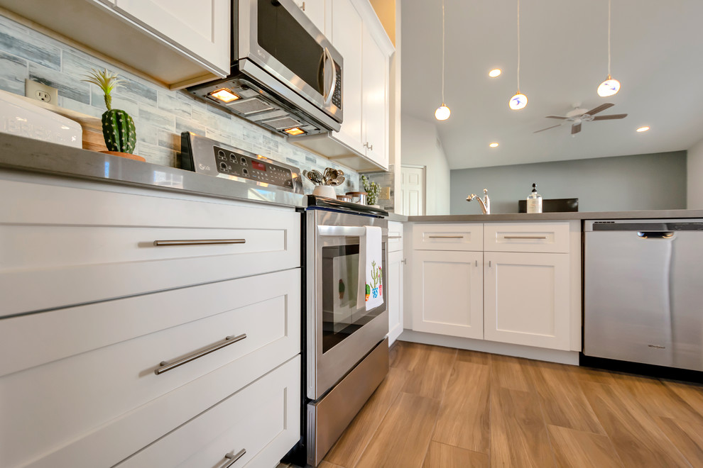 Inredning av ett modernt mellanstort grå grått kök, med en undermonterad diskho, skåp i shakerstil, vita skåp, bänkskiva i kvarts, blått stänkskydd, stänkskydd i glaskakel, klinkergolv i porslin, en halv köksö och brunt golv