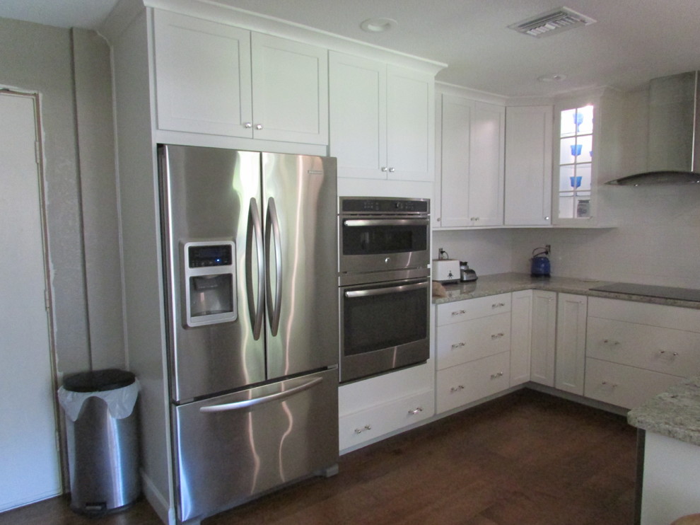 Example of a small transitional u-shaped medium tone wood floor enclosed kitchen design in Orlando with a farmhouse sink, shaker cabinets, white cabinets, granite countertops, white backsplash, ceramic backsplash, stainless steel appliances and no island