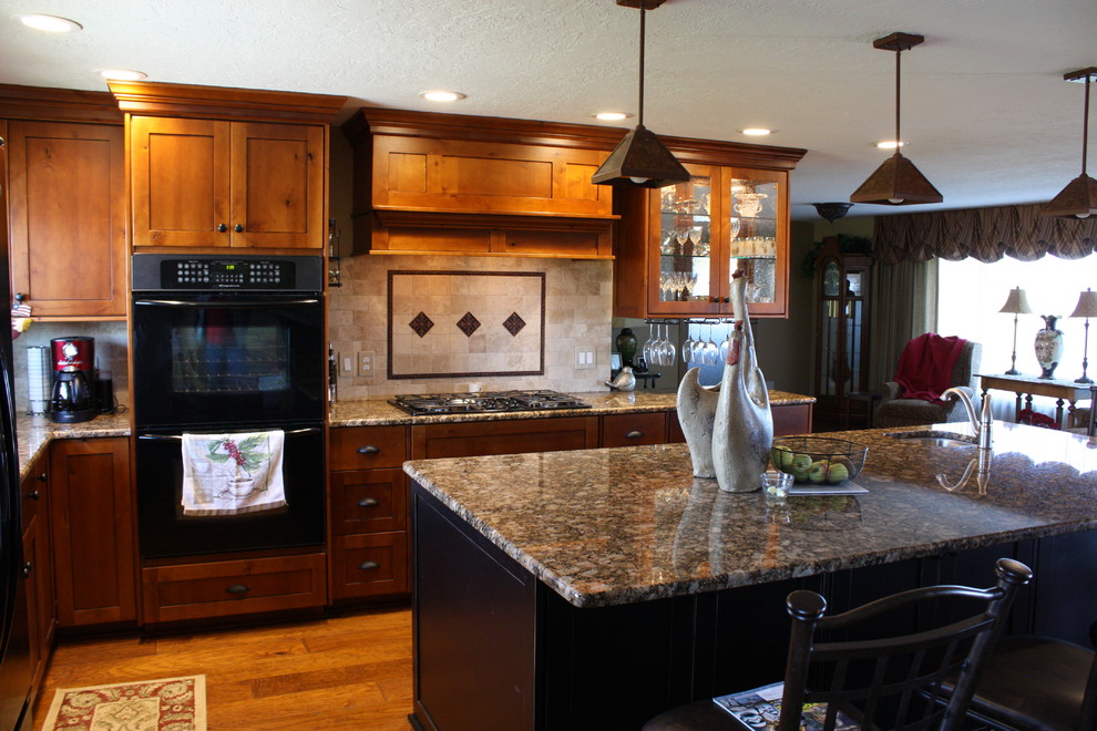 Foto di una cucina moderna chiusa e di medie dimensioni con lavello da incasso, ante di vetro, ante in legno bruno, top in granito, paraspruzzi beige, paraspruzzi con piastrelle in pietra e elettrodomestici in acciaio inossidabile