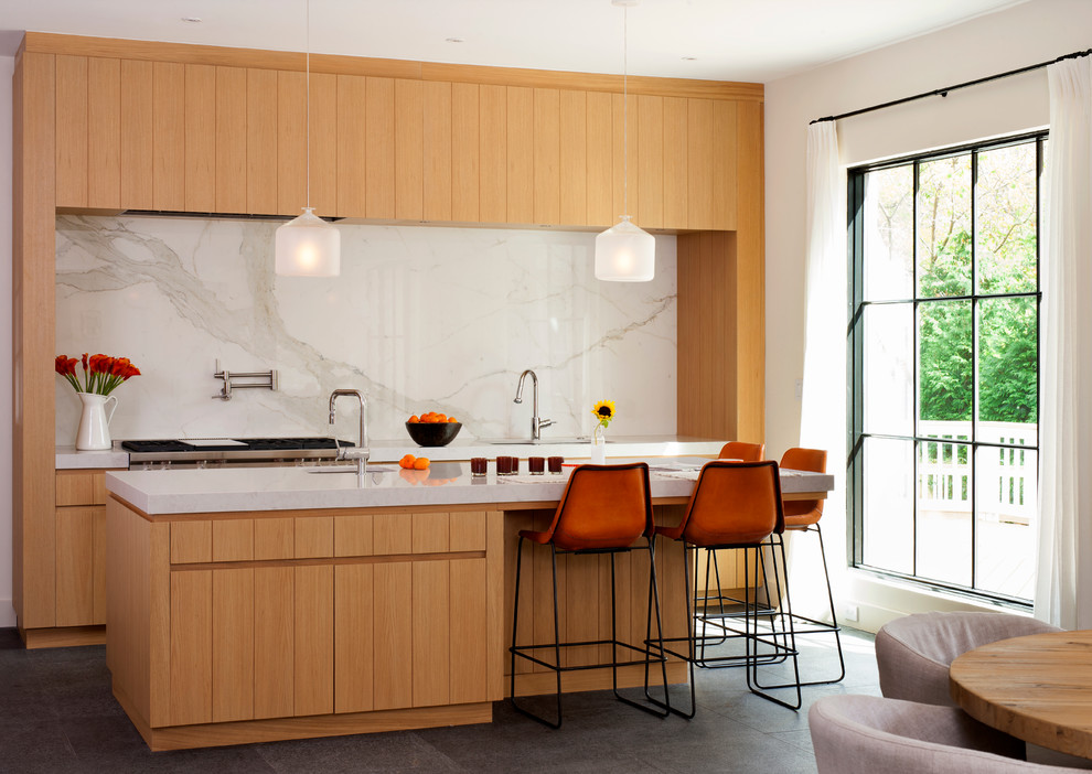 На фото: кухня в современном стиле с обеденным столом, плоскими фасадами, фасадами цвета дерева среднего тона, белым фартуком, островом и фартуком из мрамора с