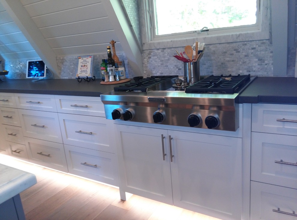 This is an example of a medium sized eclectic u-shaped kitchen/diner in Los Angeles with a submerged sink, shaker cabinets, white cabinets, engineered stone countertops, grey splashback, mosaic tiled splashback, stainless steel appliances, medium hardwood flooring, an island and brown floors.