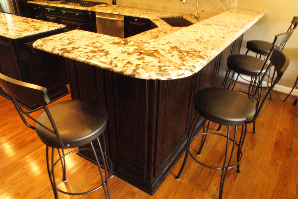 Example of a large minimalist galley medium tone wood floor and brown floor home bar design in DC Metro with an undermount sink, raised-panel cabinets, dark wood cabinets, granite countertops, beige backsplash, stone tile backsplash and beige countertops