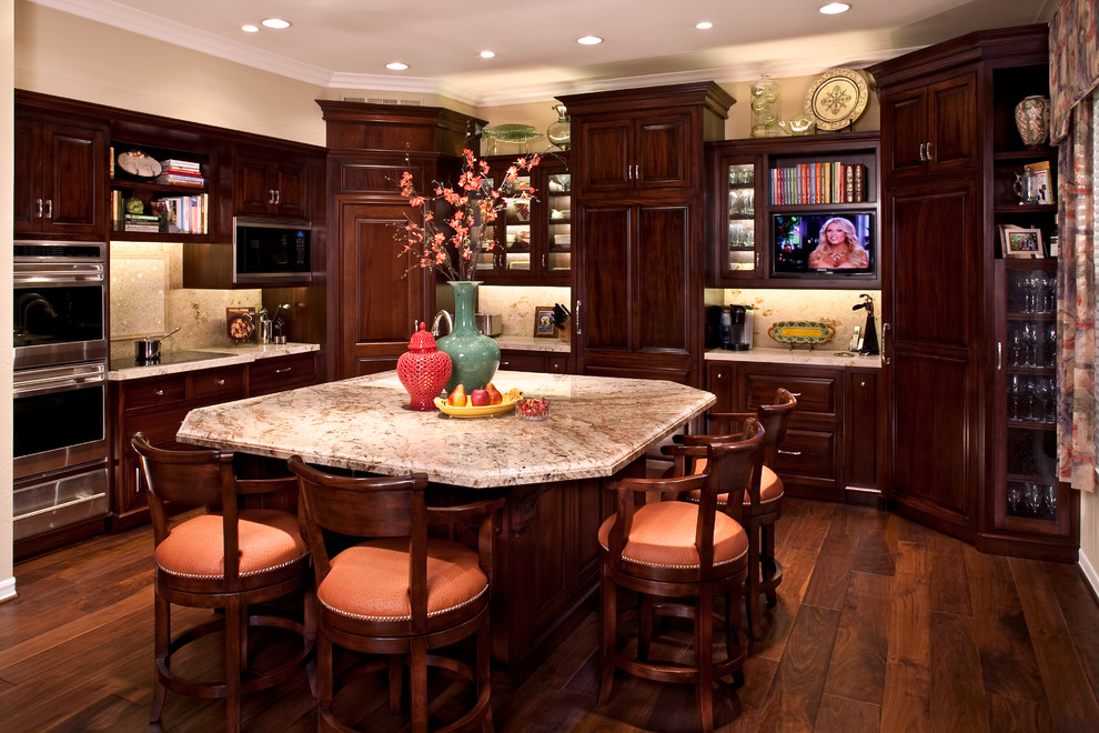 Example of a large classic l-shaped dark wood floor and brown floor eat-in kitchen design in Orange County with raised-panel cabinets, dark wood cabinets, granite countertops, beige backsplash, stone slab backsplash, stainless steel appliances and an island
