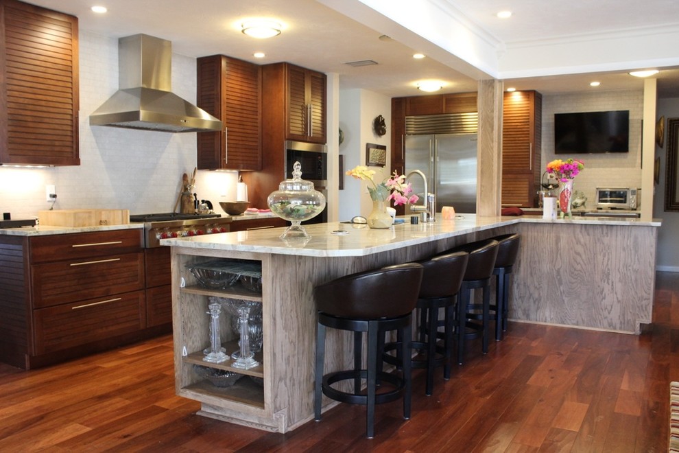 Example of a transitional l-shaped medium tone wood floor open concept kitchen design in Orlando with louvered cabinets, dark wood cabinets, granite countertops, stainless steel appliances, an island, an undermount sink, white backsplash, glass tile backsplash and white countertops