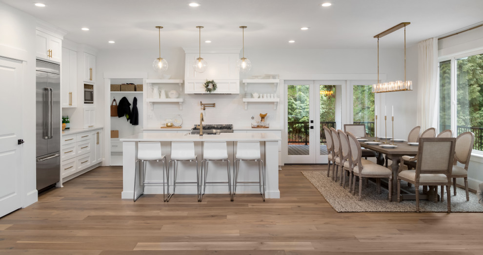 Design ideas for a medium sized contemporary l-shaped kitchen/diner in San Francisco with shaker cabinets, white cabinets, white splashback, metro tiled splashback, stainless steel appliances, medium hardwood flooring, an island, brown floors and white worktops.