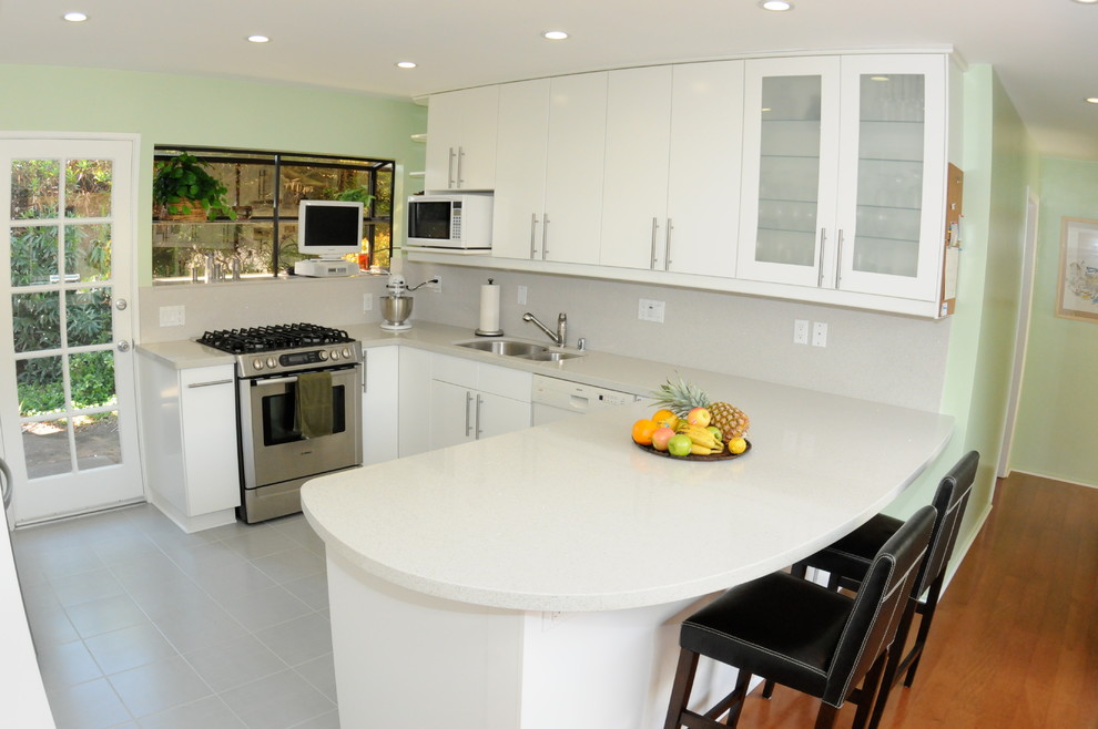 Example of a mid-sized minimalist u-shaped ceramic tile open concept kitchen design in San Diego with a double-bowl sink, flat-panel cabinets, white cabinets, quartz countertops, white backsplash, stone slab backsplash, stainless steel appliances and an island