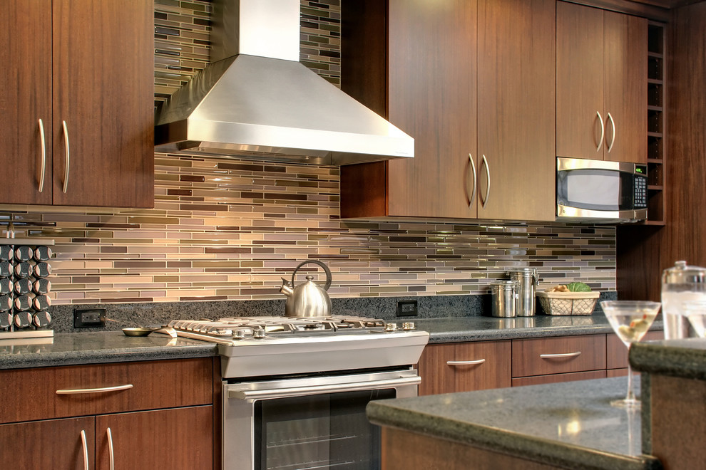 Foto de cocina contemporánea con electrodomésticos de acero inoxidable, armarios con paneles lisos, puertas de armario de madera en tonos medios, salpicadero de azulejos en listel y salpicadero multicolor