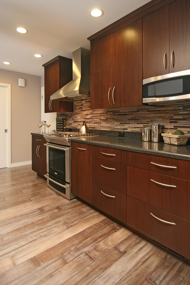 Bild på ett funkis kök, med rostfria vitvaror, släta luckor, skåp i mörkt trä, stänkskydd i stickkakel och flerfärgad stänkskydd