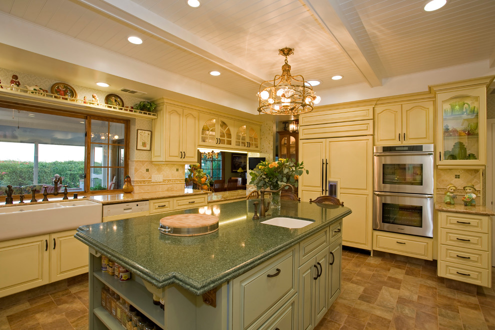 Enclosed kitchen - large traditional u-shaped porcelain tile enclosed kitchen idea in San Diego with a farmhouse sink, raised-panel cabinets, yellow cabinets, granite countertops, beige backsplash, stone tile backsplash, paneled appliances and an island