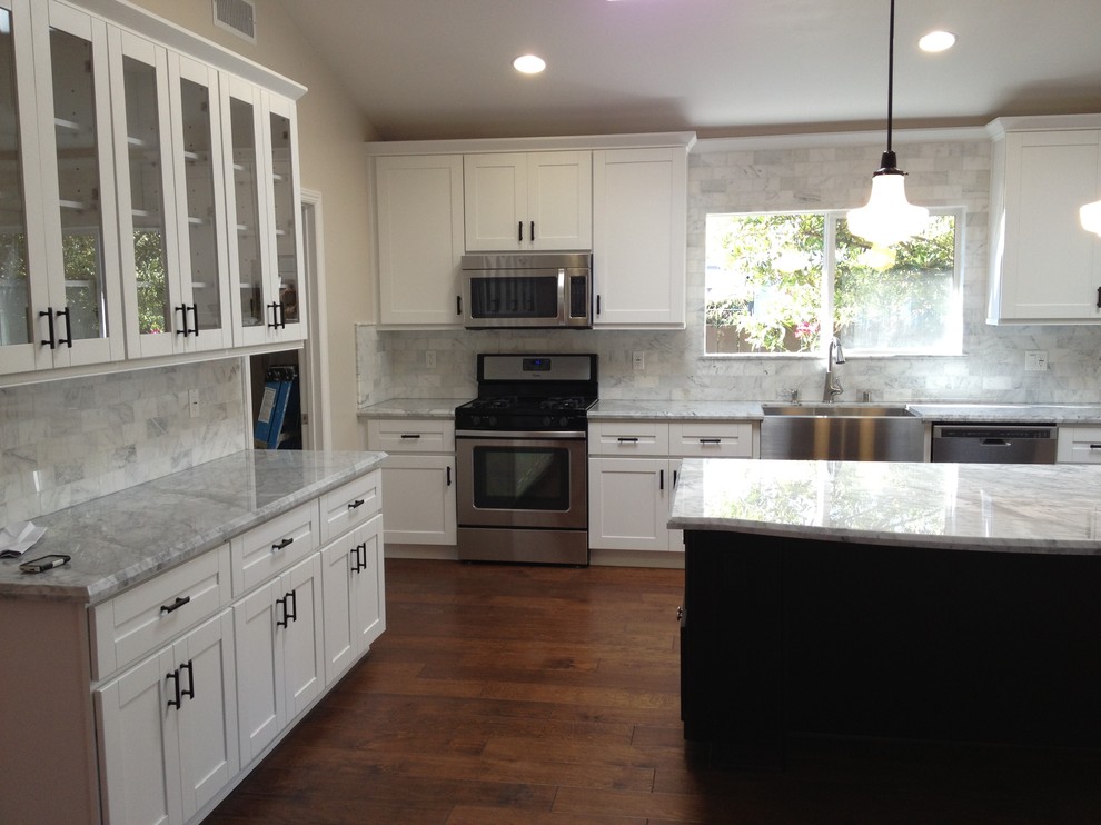 Inspiration for a large country u-shaped brown floor and medium tone wood floor eat-in kitchen remodel in San Francisco with a farmhouse sink, shaker cabinets, white cabinets, gray backsplash, stone tile backsplash, stainless steel appliances, an island, quartz countertops and gray countertops