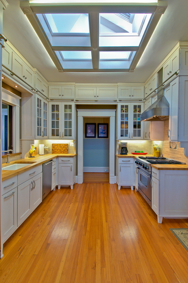 Inredning av ett klassiskt avskilt kök, med en undermonterad diskho, luckor med infälld panel, vita skåp, rostfria vitvaror och träbänkskiva