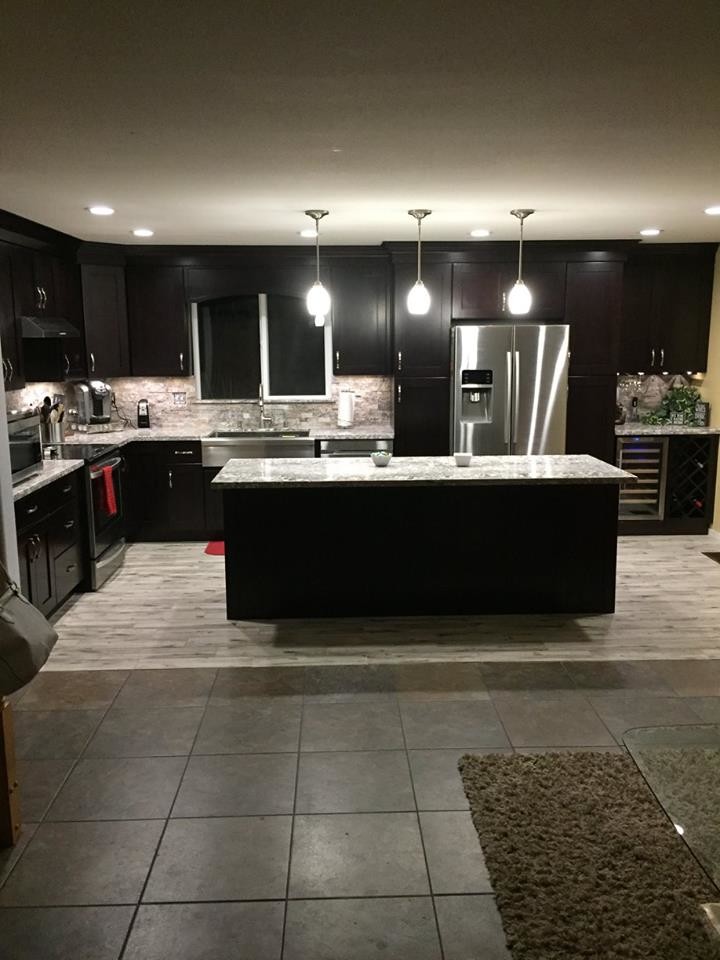 Modern inredning av ett mellanstort kök, med en undermonterad diskho, svarta skåp, granitbänkskiva, grått stänkskydd, stänkskydd i travertin, rostfria vitvaror, en köksö och grått golv